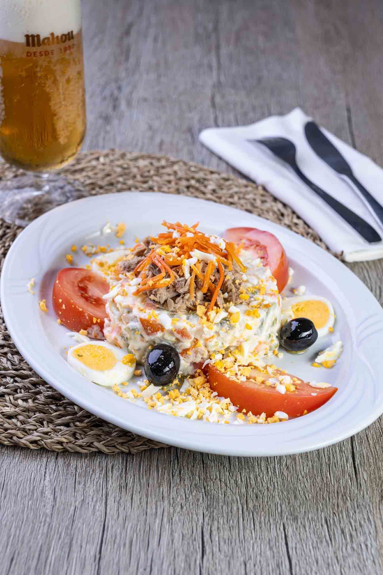 Un plato de comida con tomates, huevos y aceitunas en una mesa junto a un vaso de cerveza.