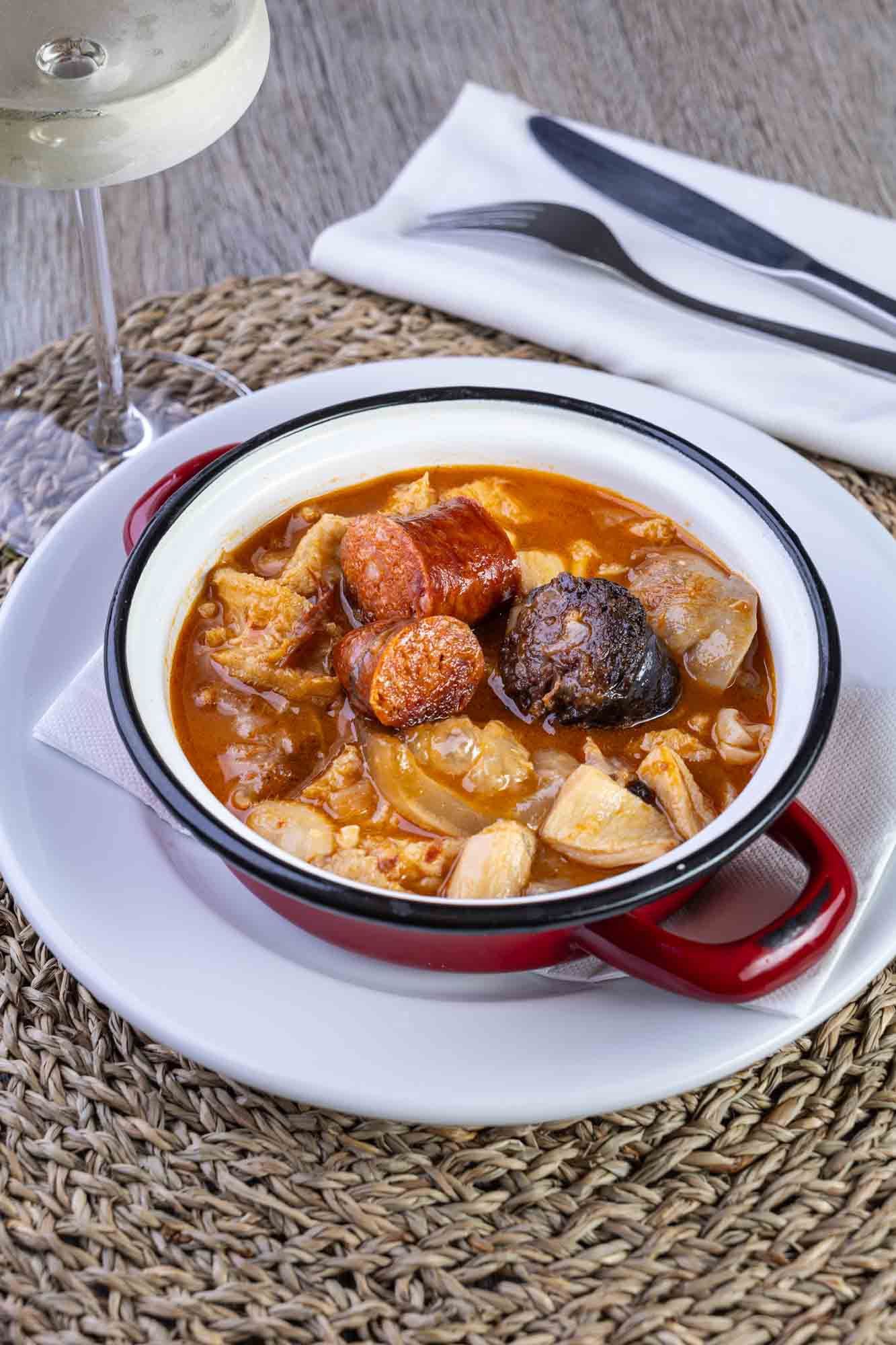 En un plato hay un plato de guiso junto a una copa de vino.