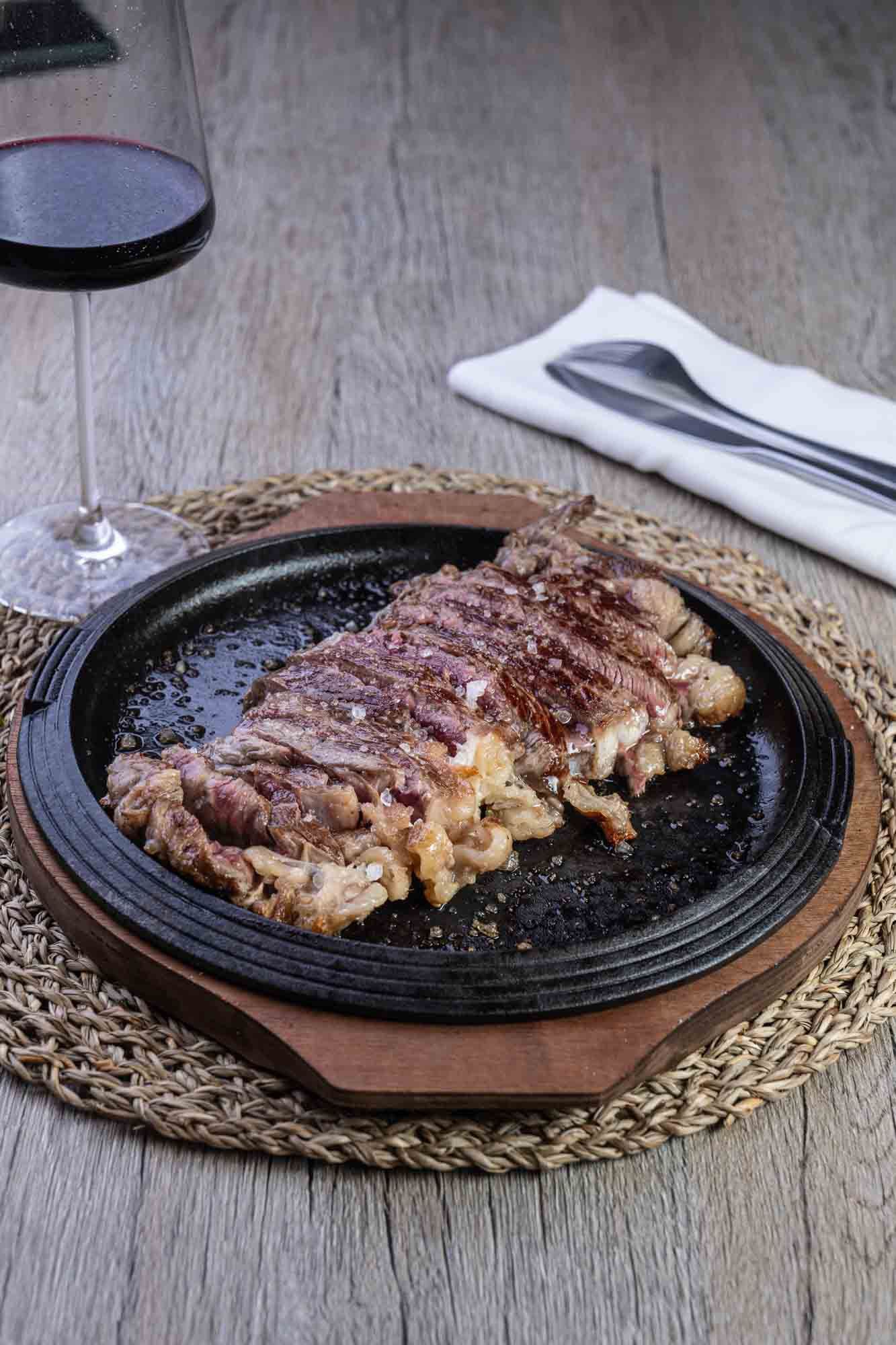 Un filete está sentado en un plato sobre una mesa de madera al lado de una copa de vino.