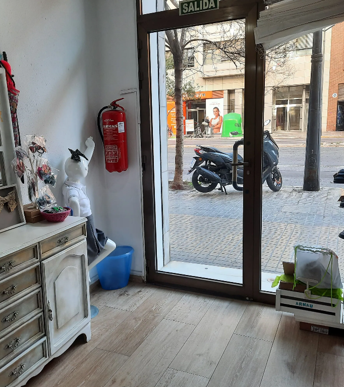 Puerta interior de tienda con extintor, scooter visible a través de puerta de vidrio.