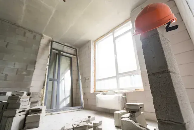 Interior de construcción: casco naranja sobre una columna de hormigón; paredes y ventanas sin terminar.