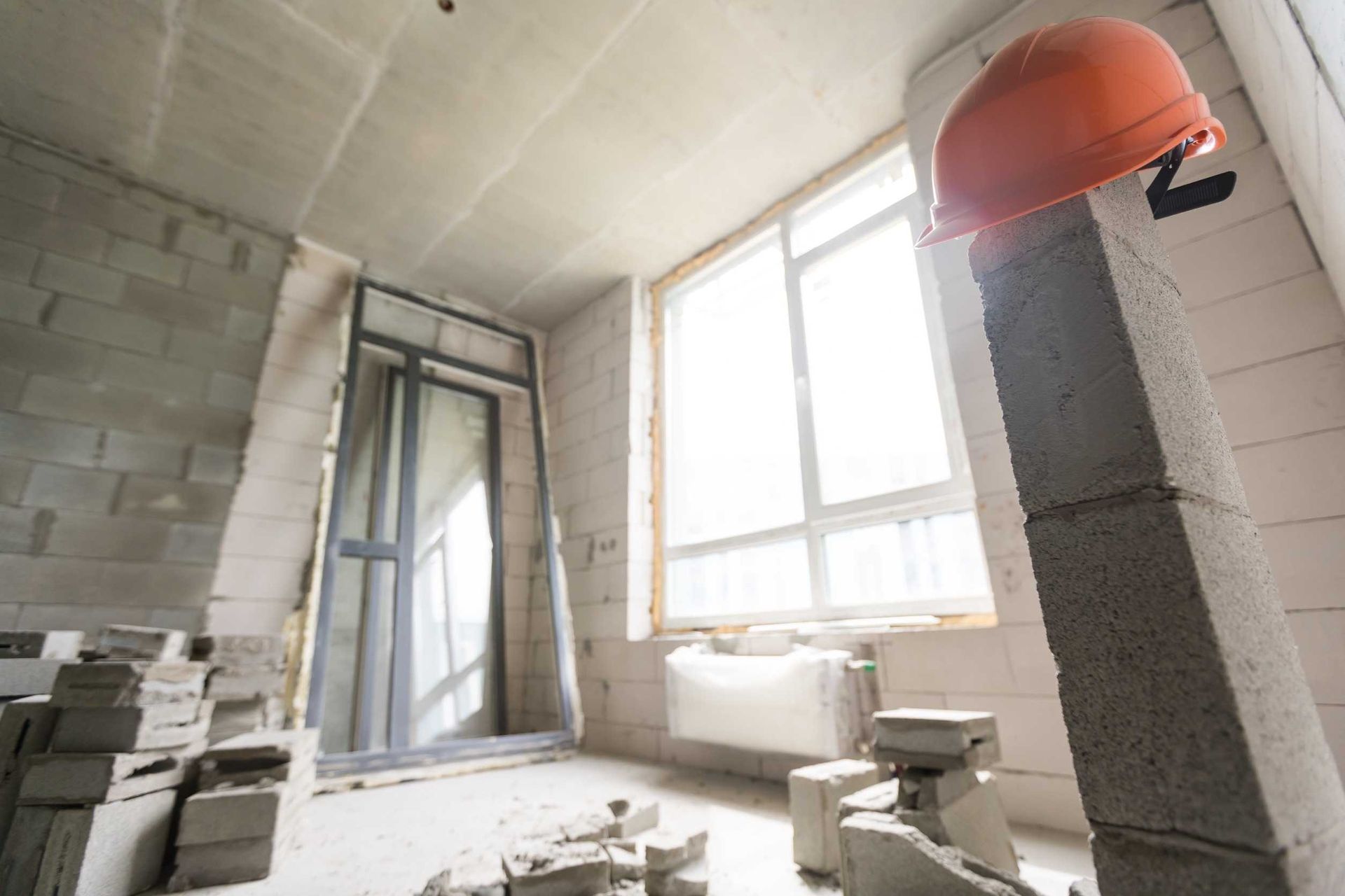 Sitio de construcción interior con casco naranja sobre pilar, ventana y bloques de hormigón.