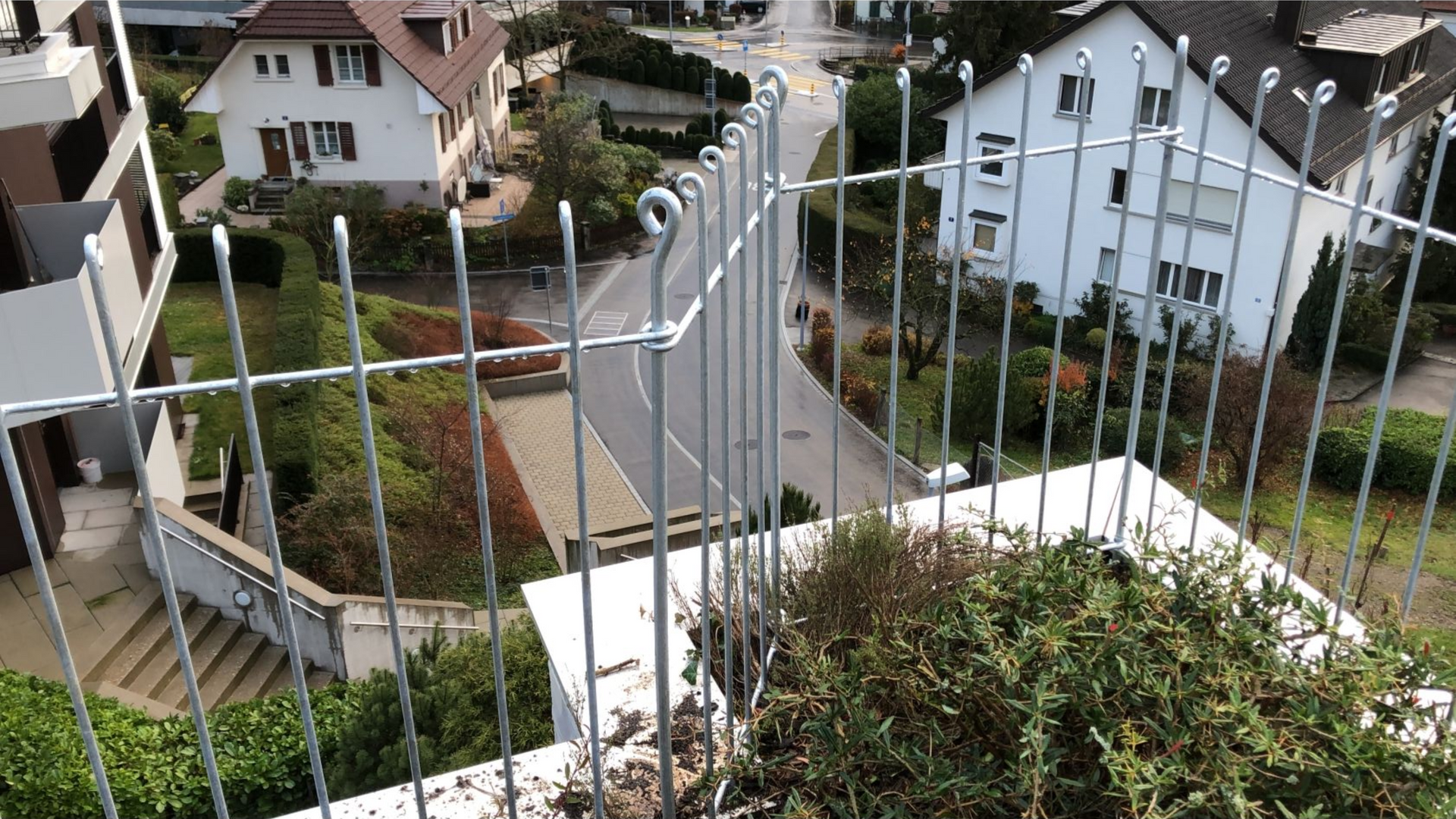 Blick von einem Balkon mit Metallgeländer auf eine Straße und Häuser.