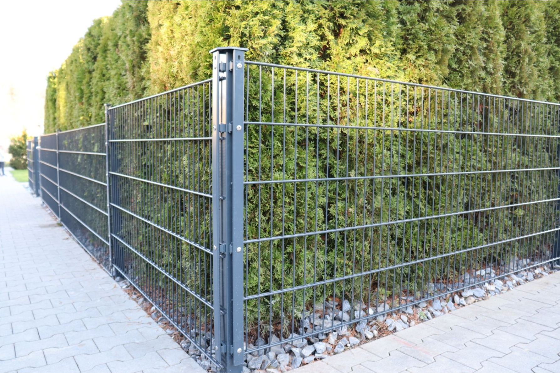 Schwarzer Metallzaun entlang einer Reihe grüner Büsche und Bäume in einem Wohngebiet.