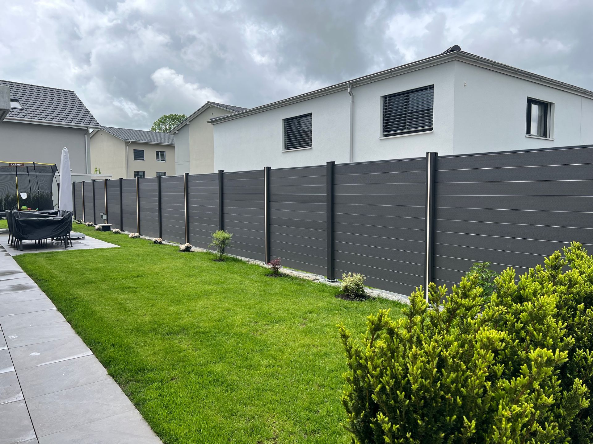 An einem bewölkten Tag umgibt ein dunkelgrauer horizontaler Lattenzaun einen üppigen grünen Rasen neben einem Haus.