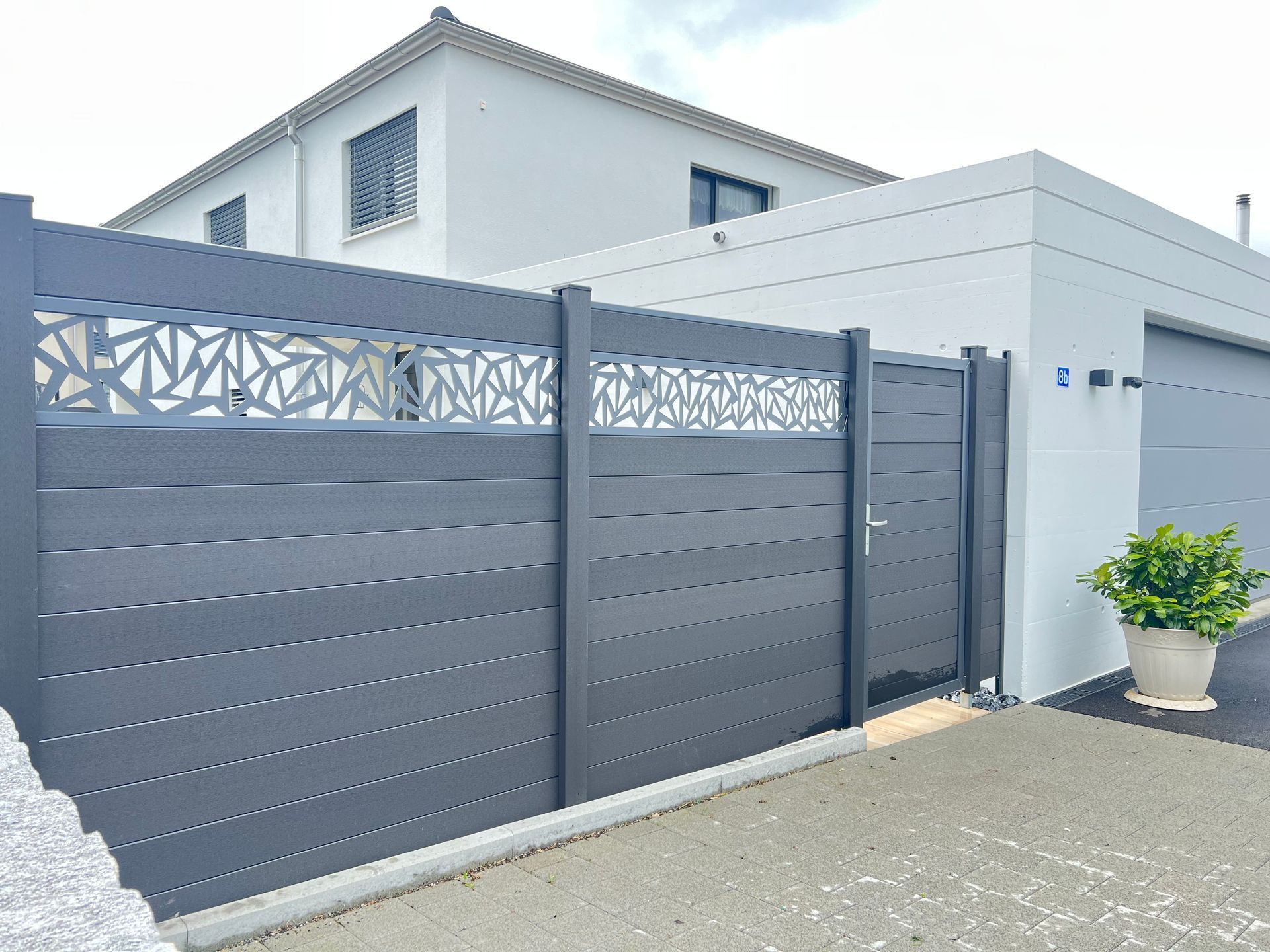 Grauer Metallzaun mit dekorativem Oberteil und passendem Tor vor einem weißen Haus.