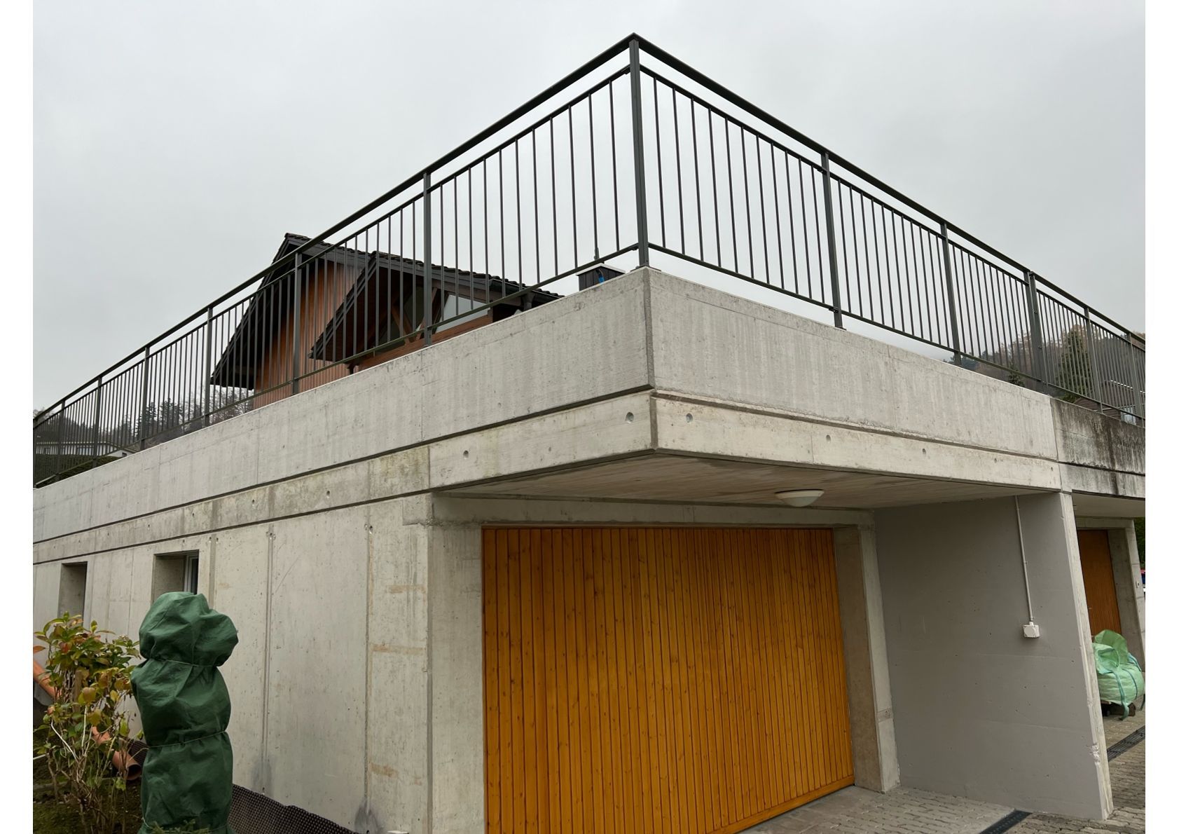 Modernes Gebäude mit Betonfassade und schwarzem Metallgeländer; Garagentore aus Holz.