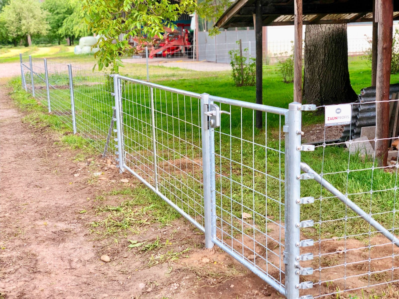 Metalltor und Zaun vor einer Rasenfläche, in der Nähe von Bäumen und einem Gebäude.