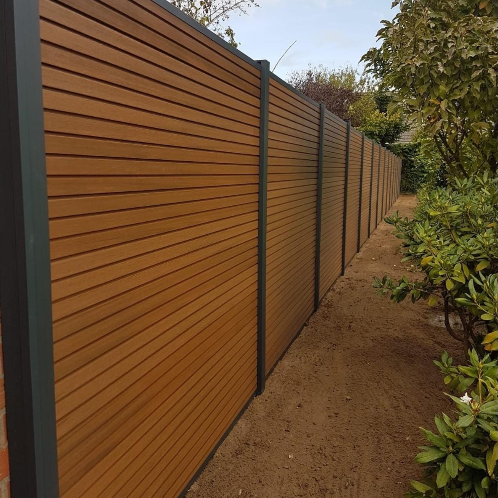 Ein langer, brauner horizontaler Lattenzaun mit dunkelgrauen Pfosten; in einem Garten.