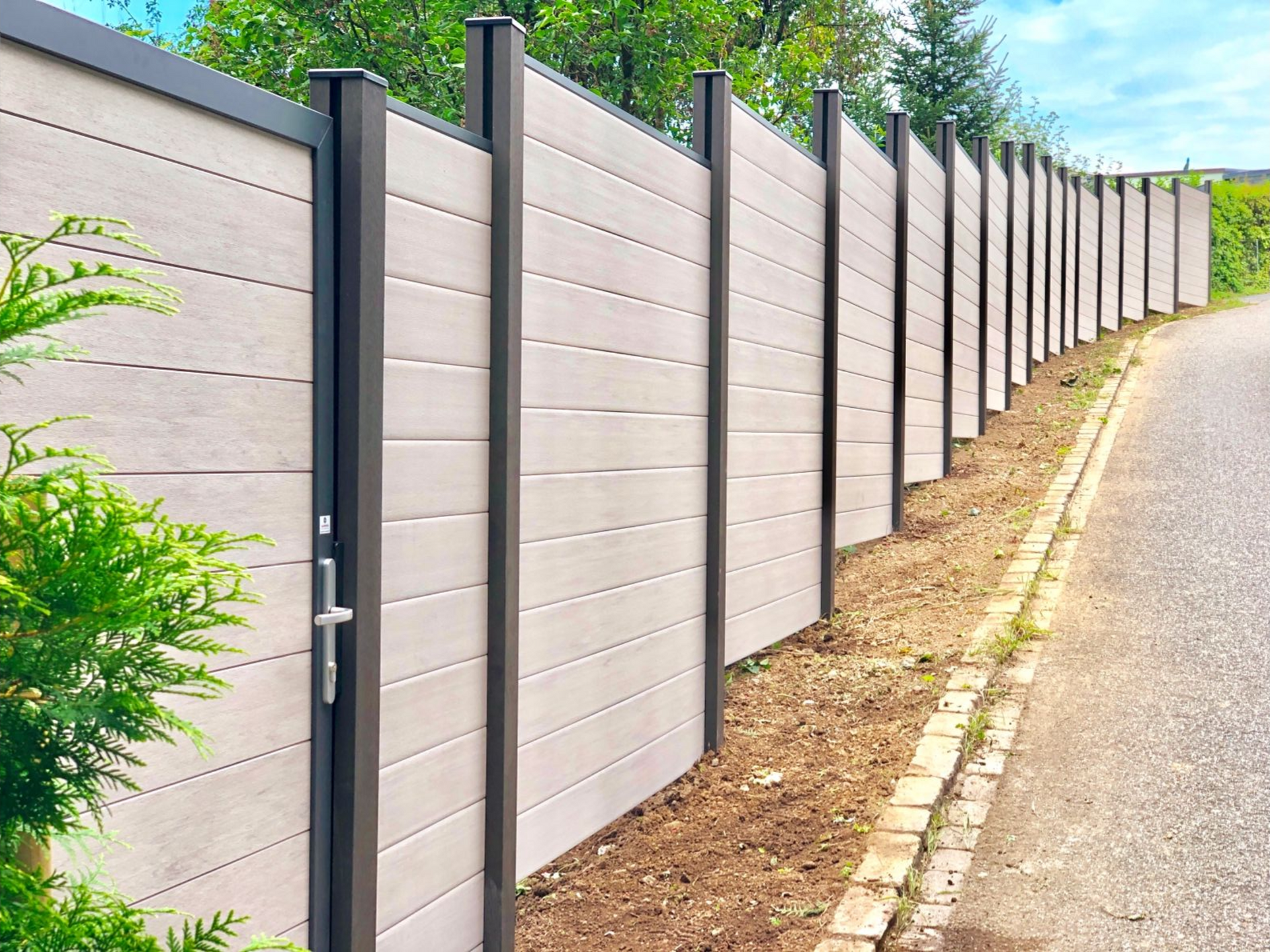 Beiger und dunkelgrauer Sichtschutzzaun aus Verbundwerkstoff entlang einer Straße.