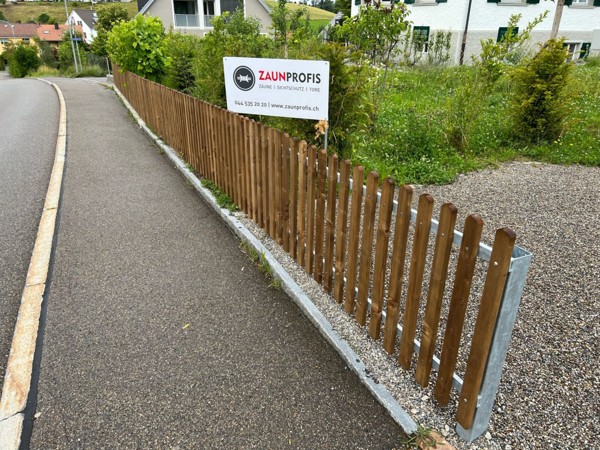 Holzzaun entlang eines Bürgersteigs mit einem Schild für TAUMBOR'S.
