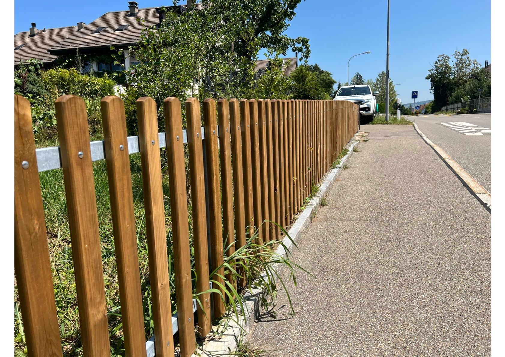 Holzlattenzaun neben einer Straße, im Hintergrund ein Auto.