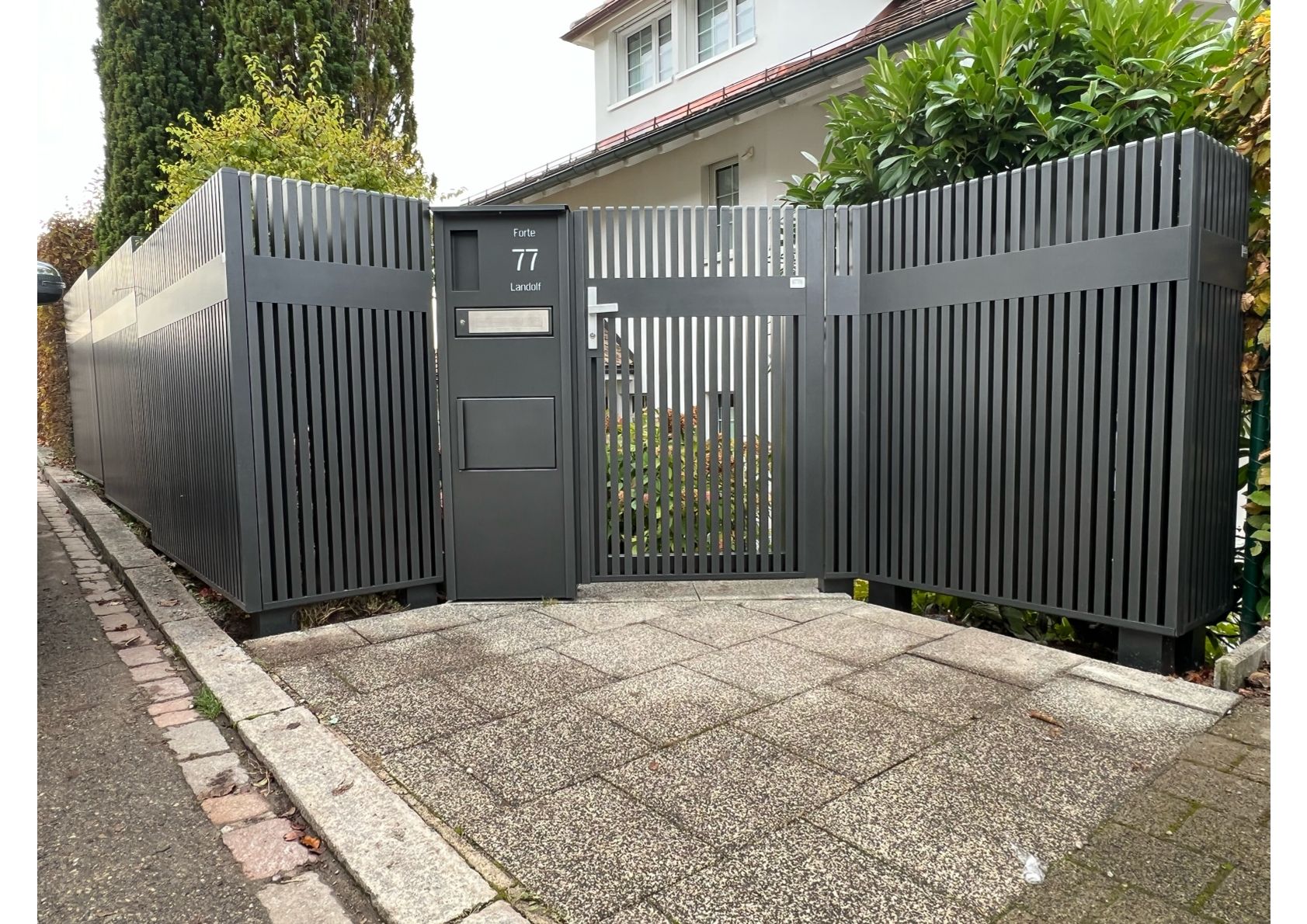 Dunkelgrauer moderner Zaun und Tor vor einem Haus.