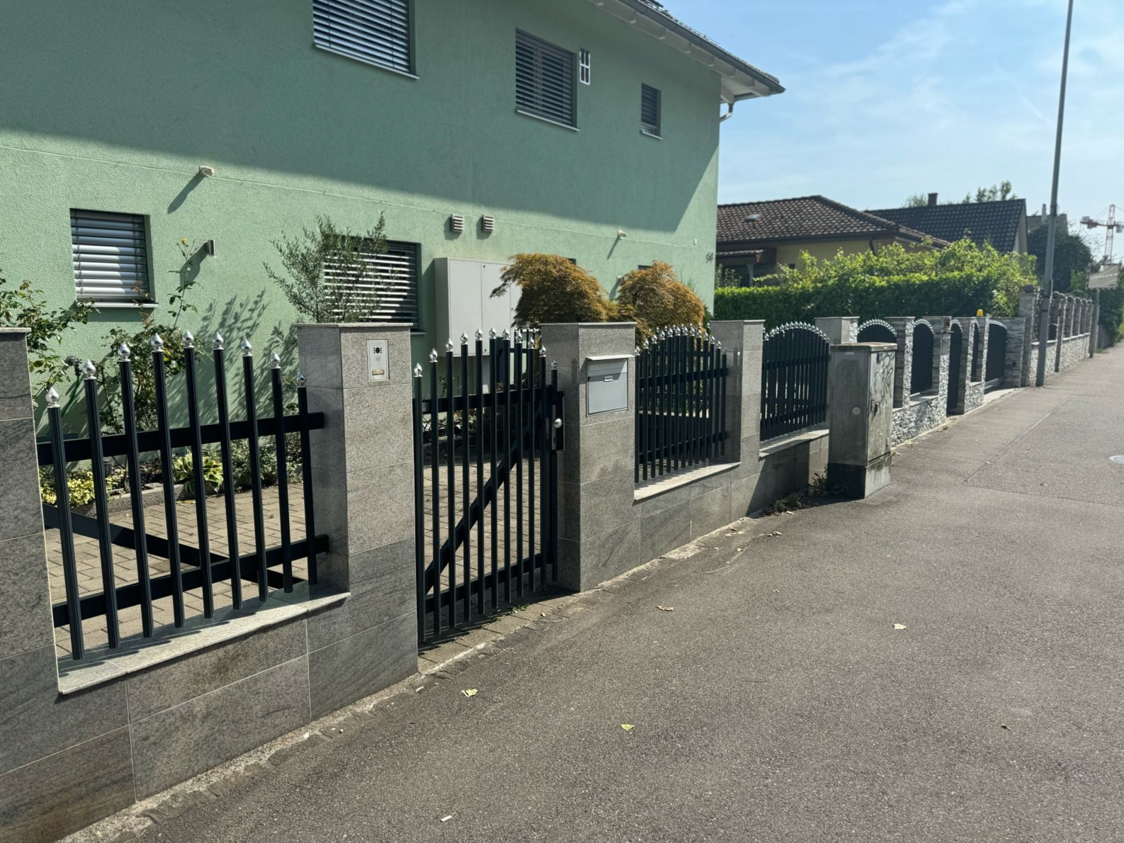 Grünes Haus mit grauem Steinzaun und schwarzem Metalltor.
