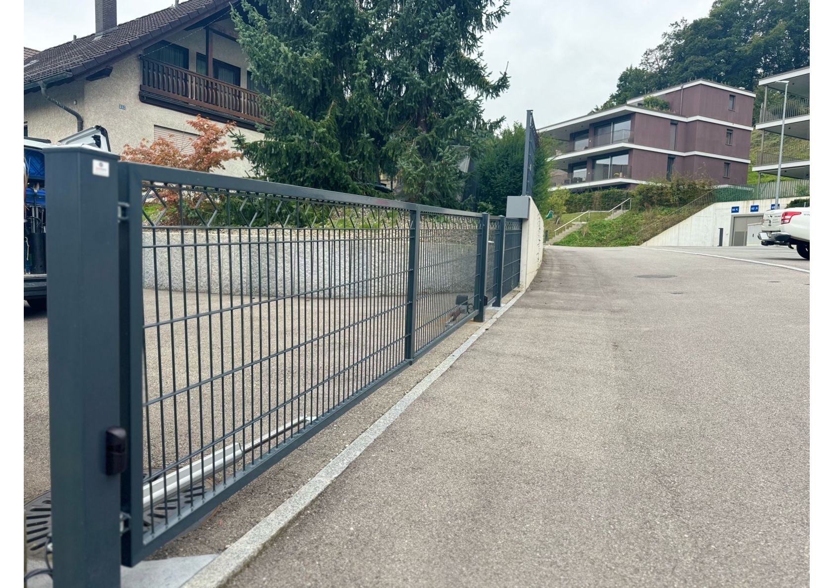 Graues Metallschiebetor blockiert eine gepflasterte Auffahrt in einem Wohngebiet.