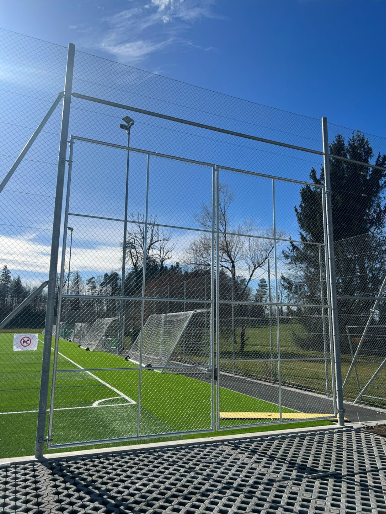 Ein eingezäuntes Fußballfeld mit grünem Rasen, Toren und klarem Himmel.