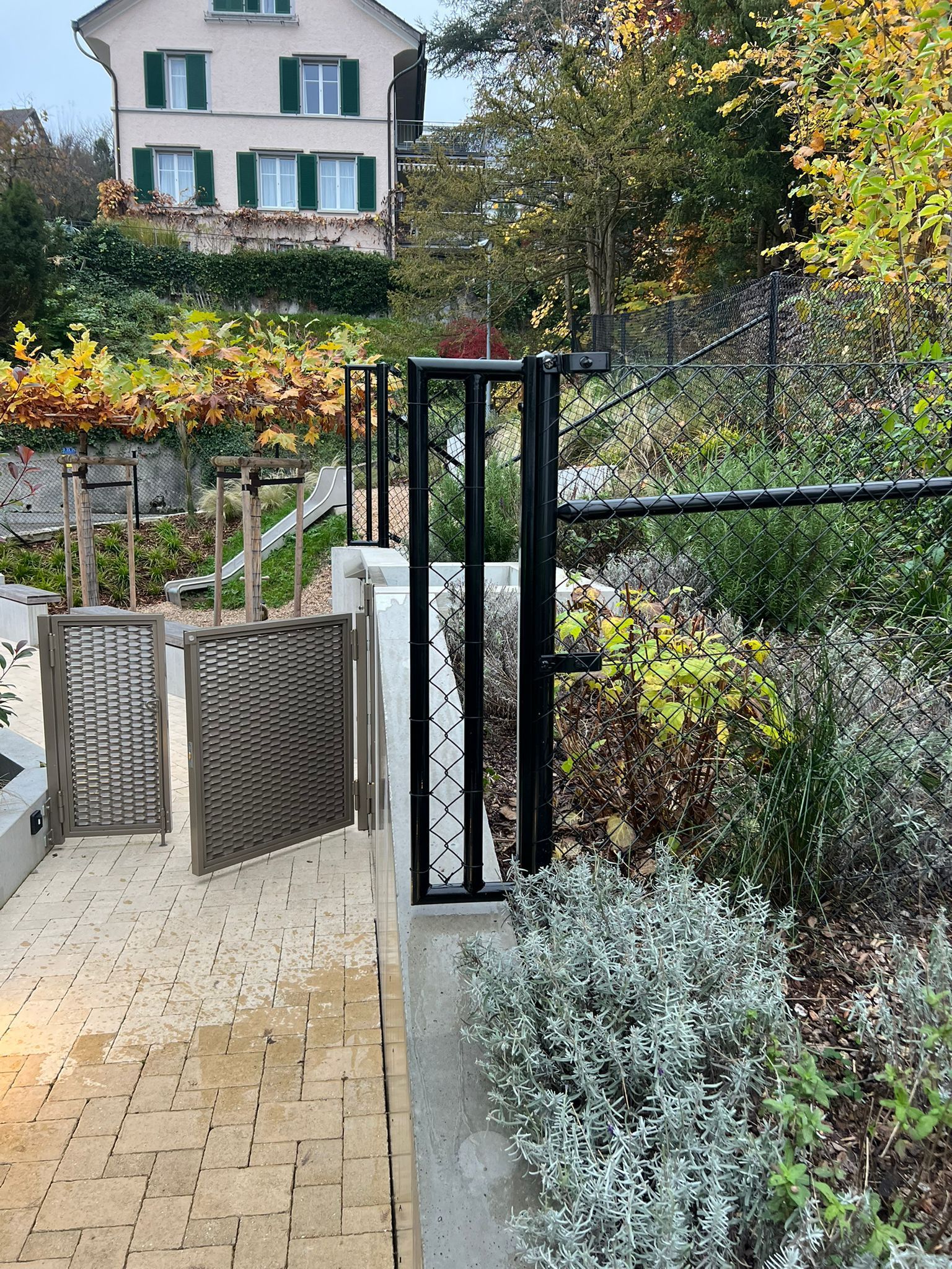 Ein schwarzes Tor und gewebte Fliegengitter führen zu einem Haus an einem Hang mit Herbstlaub.