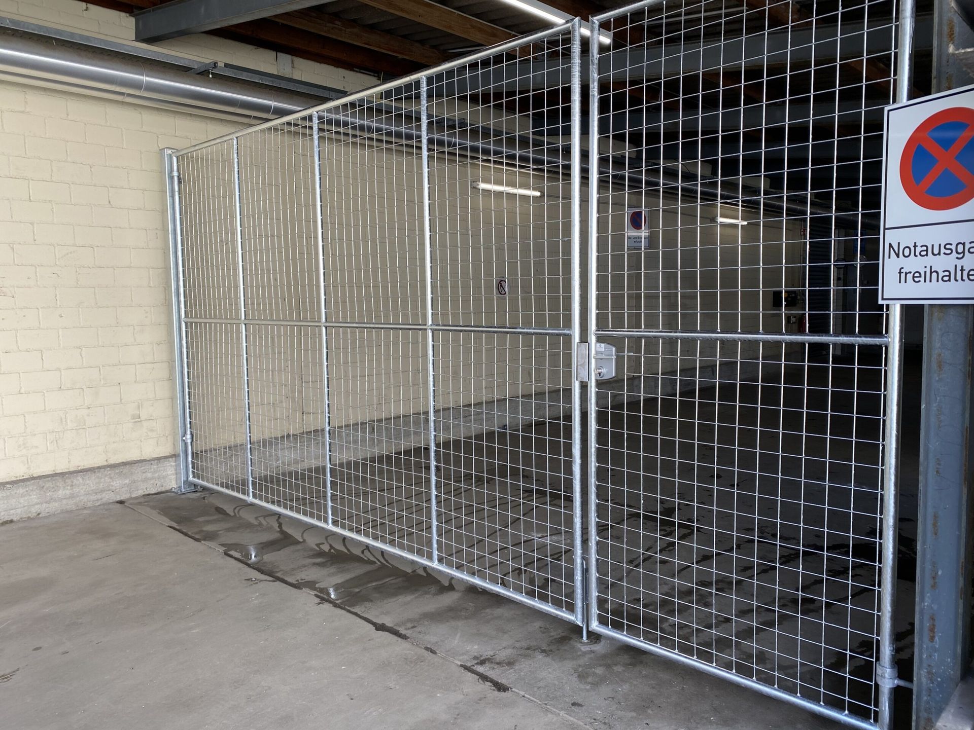 Metalltor mit einer durchsichtigen Kunststoffbarriere und einem Parkverbotsschild. Im Inneren befindet sich eine Garage.