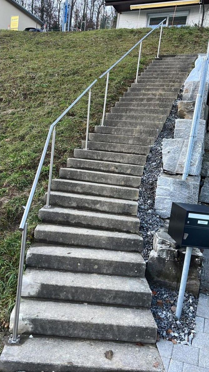 Betontreppe im Freien mit Metallhandlauf, die bergauf führt.