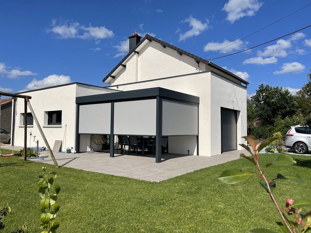 Maison blanche moderne avec des finitions noires, une grande terrasse et une pelouse sous un ciel d'un bleu éclatant