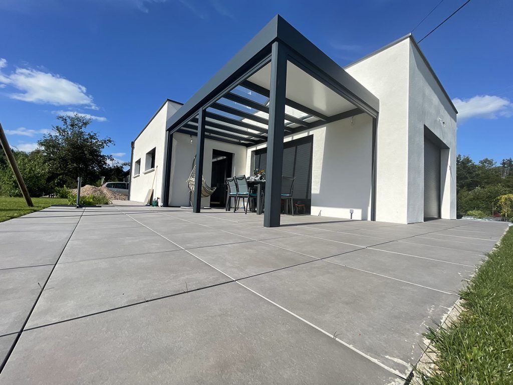 Maison blanche moderne avec patio couvert et grande allée en béton sous un ciel bleu