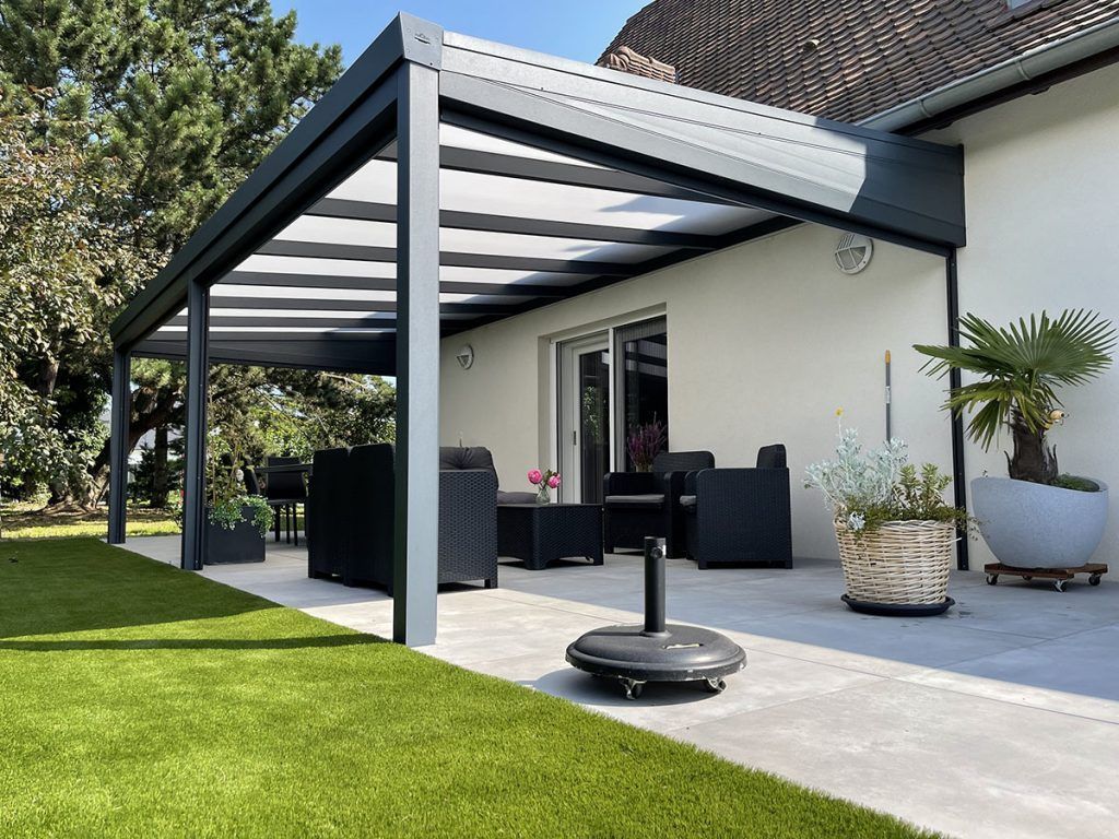 Patio moderne avec pergola noire, ensemble de salle à manger d'extérieur et pelouse à côté d'une maison blanche