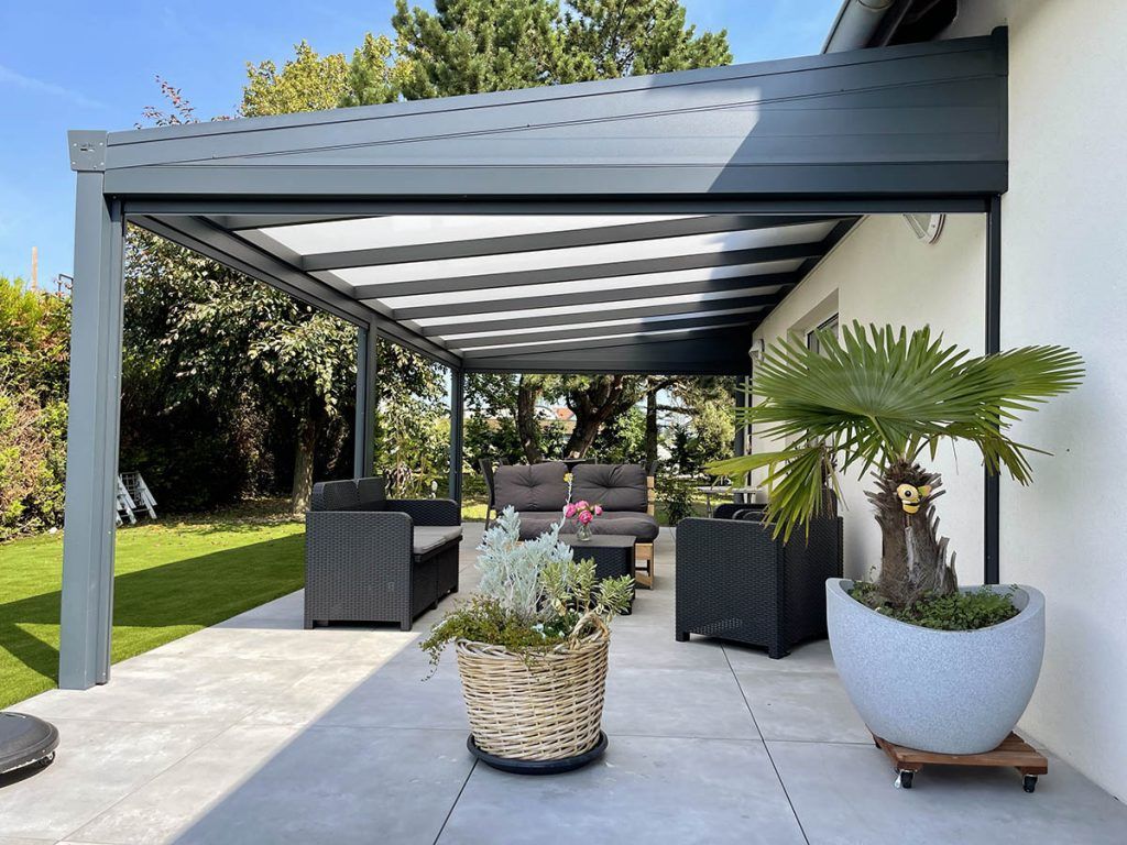 Patio moderne avec une pergola grise, des sièges d'extérieur et des plantes en pot à côté d'une pelouse