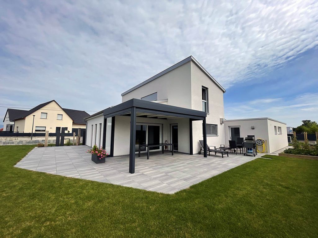 Maison blanche moderne de deux étages avec des finitions noires, une terrasse et une grande pelouse sous un ciel nuageux