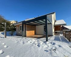 Maison moderne enneigée avec un abri voiture sous un ciel bleu clair