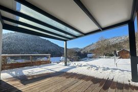 Vue sur les montagnes enneigées depuis une terrasse en bois sous un patio couvert par temps clair