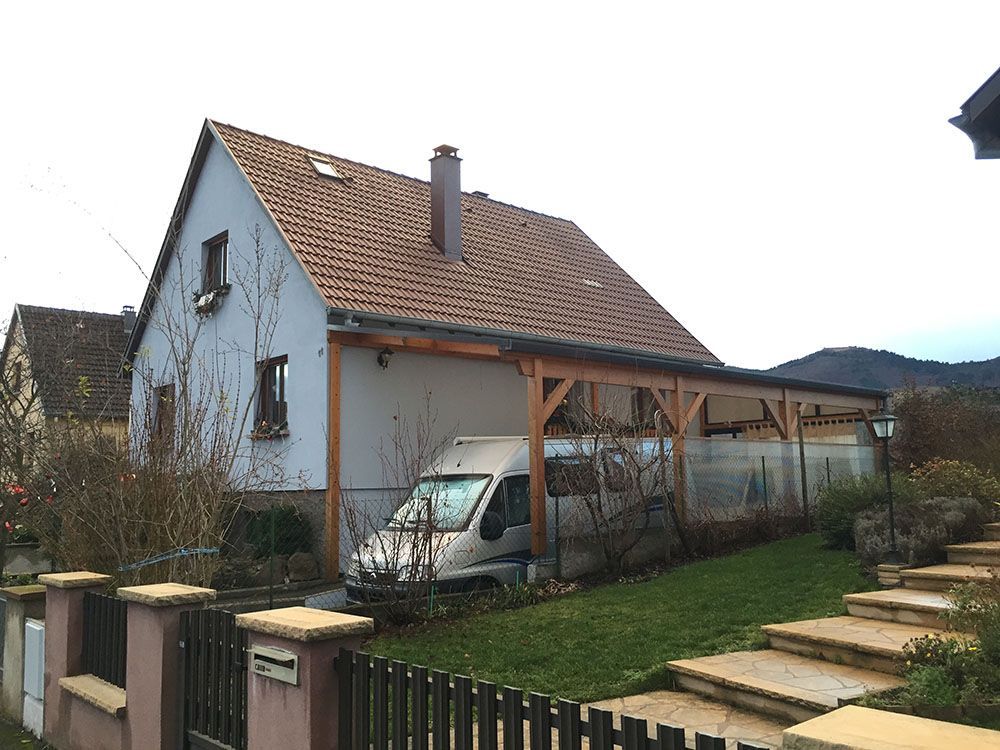 Maison au toit de tuiles rouges, allée couverte, camionnette garée et jardin en terrasses dans une cour de banlieue.