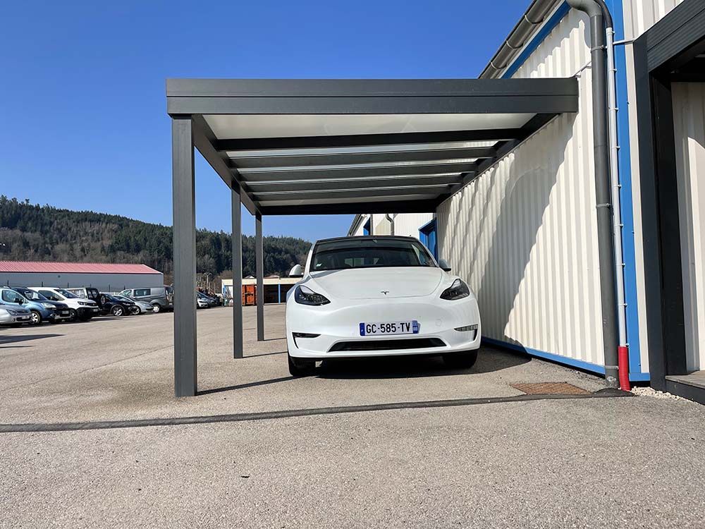 Voiture blanche garée sous un abri métallique moderne à côté d'un bâtiment par une journée ensoleillée