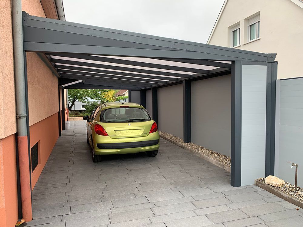 Voiture jaune garée sous un abri gris à côté d'une maison couleur pêche