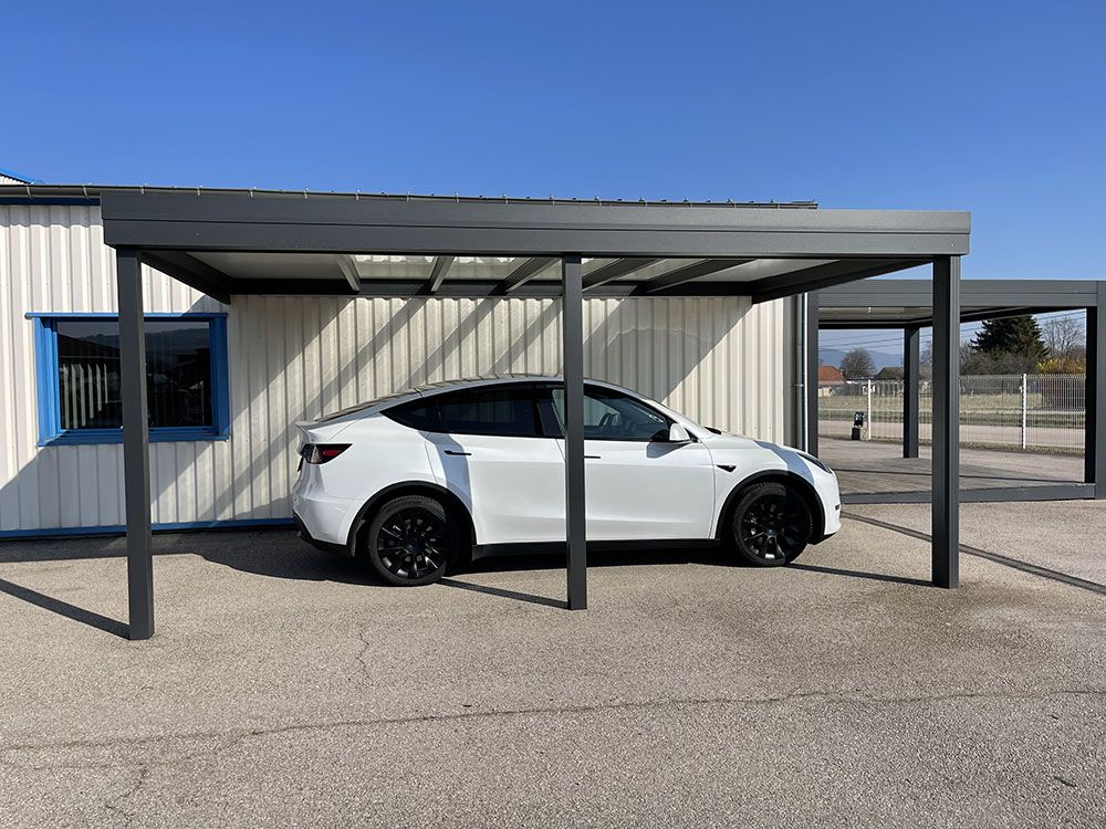 Voiture de sport blanche garée sous un abri métallique à côté d'un bâtiment en tôle ondulée par une journée ensoleillée