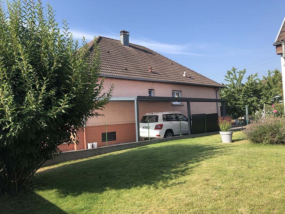 Maison de banlieue avec une voiture garée sous l'abri et une pelouse verte devant.