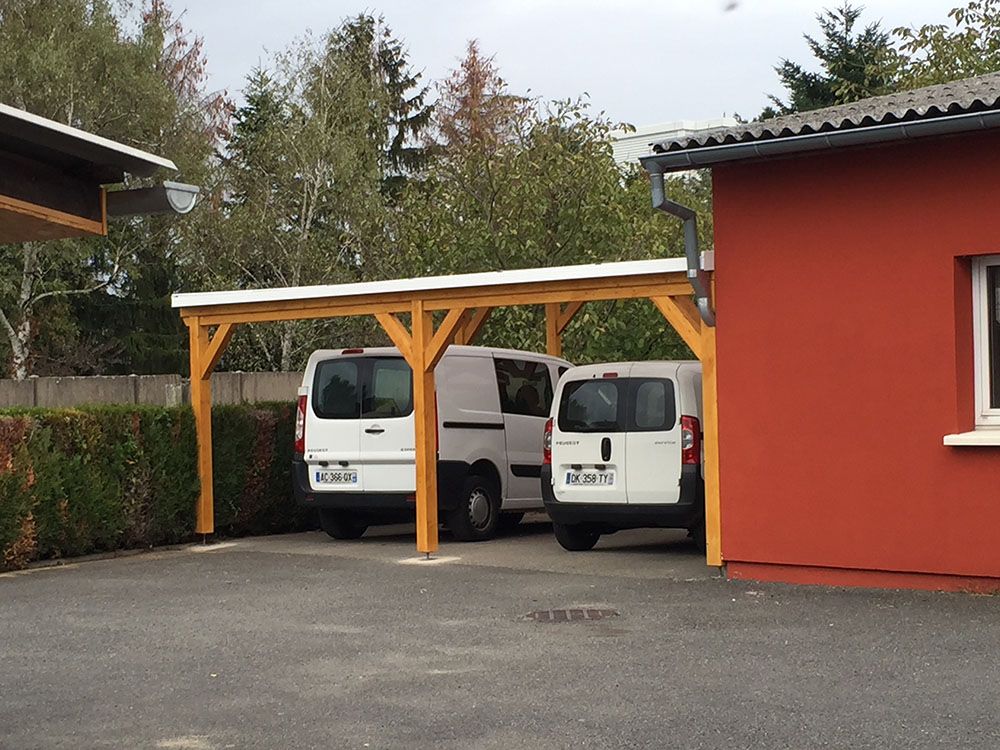 Deux camionnettes blanches garées sous un abri en bois à côté d'un bâtiment rouge.