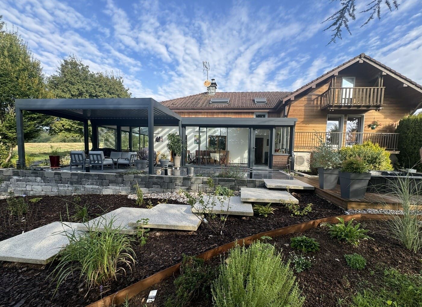 Maison moderne avec patio, pergola et jardin paysager en pierre sous un ciel bleu