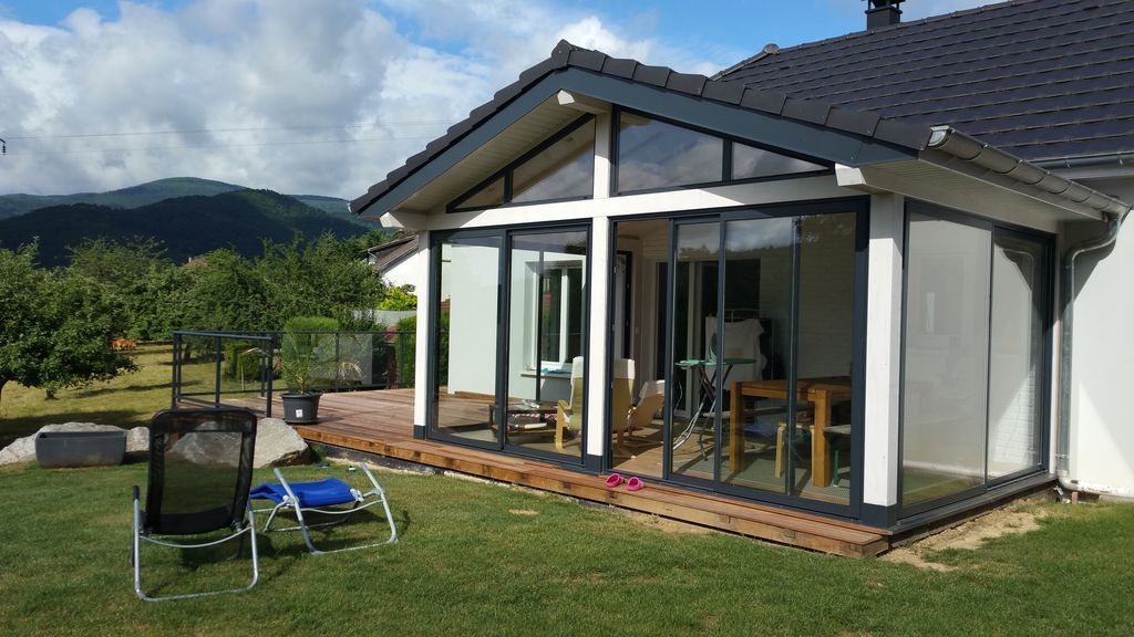 Maison moderne avec de grandes fenêtres et un patio dans un cadre montagneux verdoyant