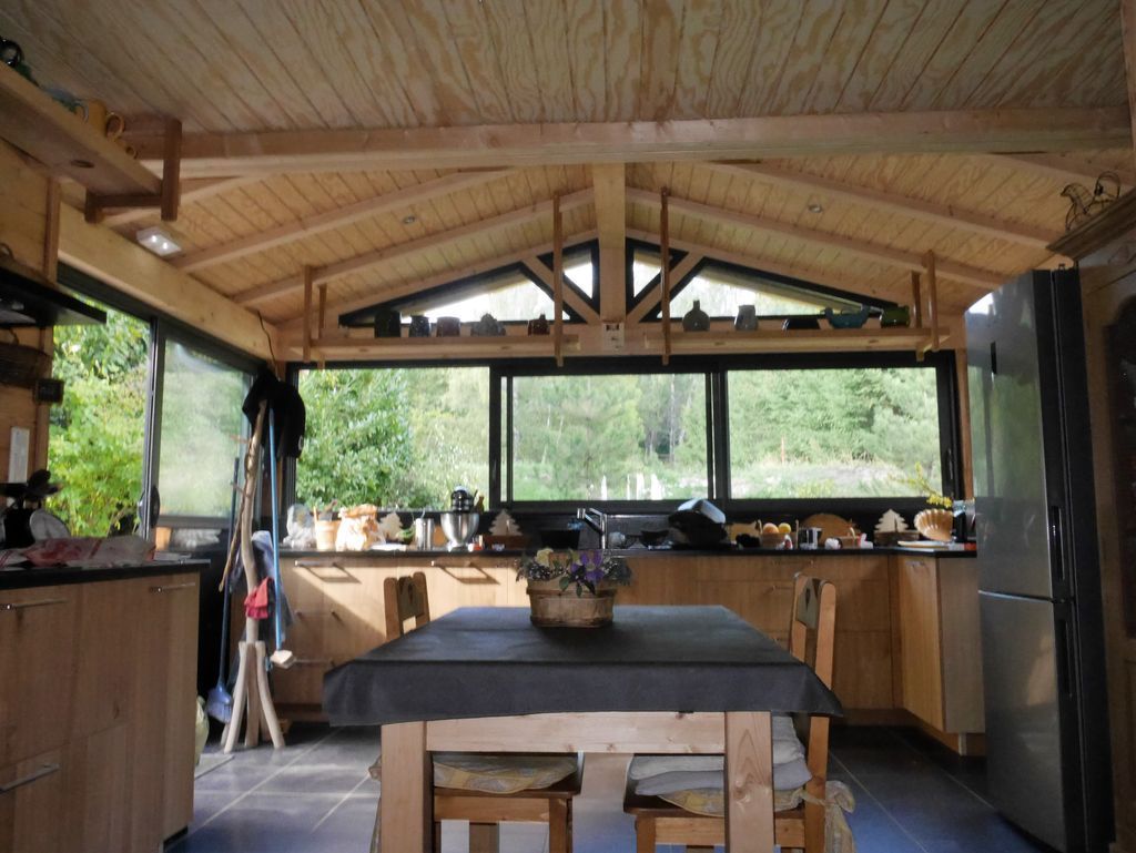 Cuisine extérieure en bois avec table à manger, placards, évier, barbecue et réfrigérateur en inox sous un toit couvert