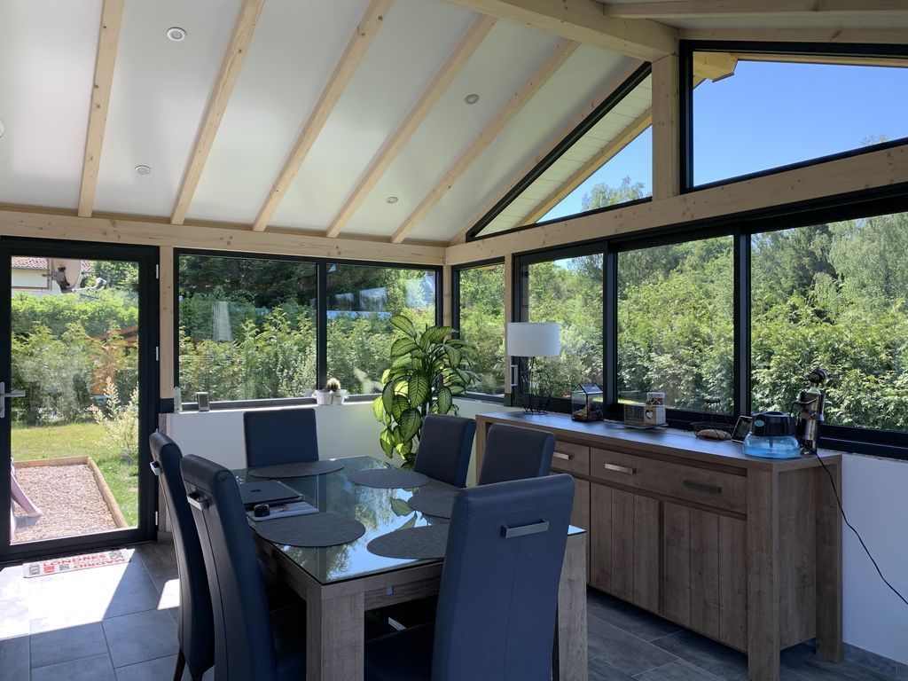 Salle à manger lumineuse de type véranda avec parois vitrées, table, chaises et buffet donnant sur un jardin