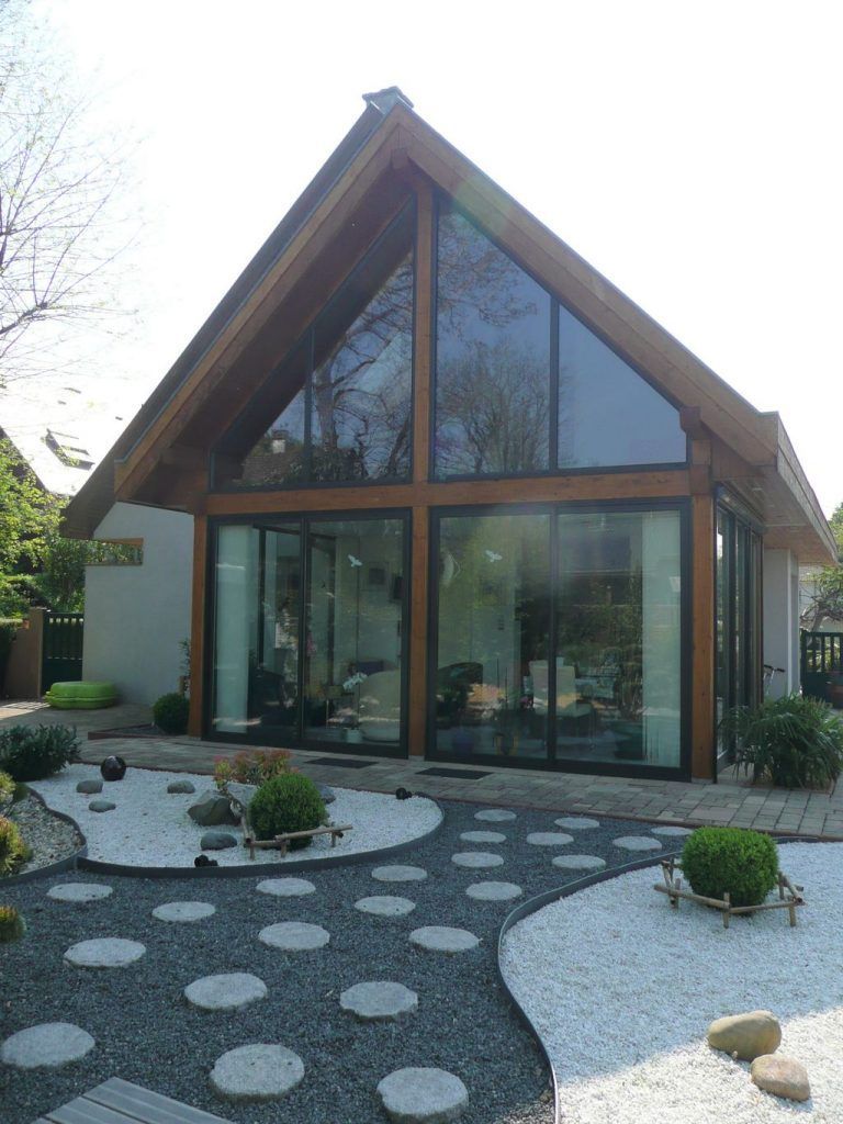 Maison moderne de type A avec de grandes baies vitrées et une cour avant paysagée avec chemin de pierre et gravier.