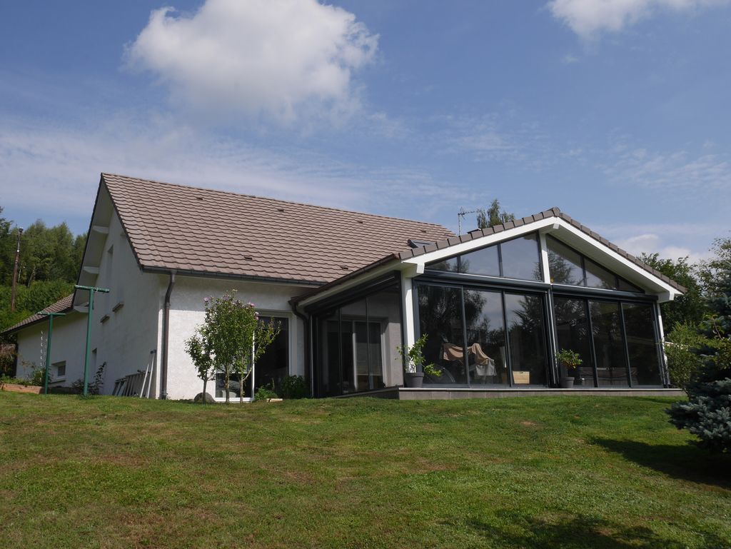 Maison blanche avec une grande véranda vitrée sur une colline herbeuse sous un ciel bleu