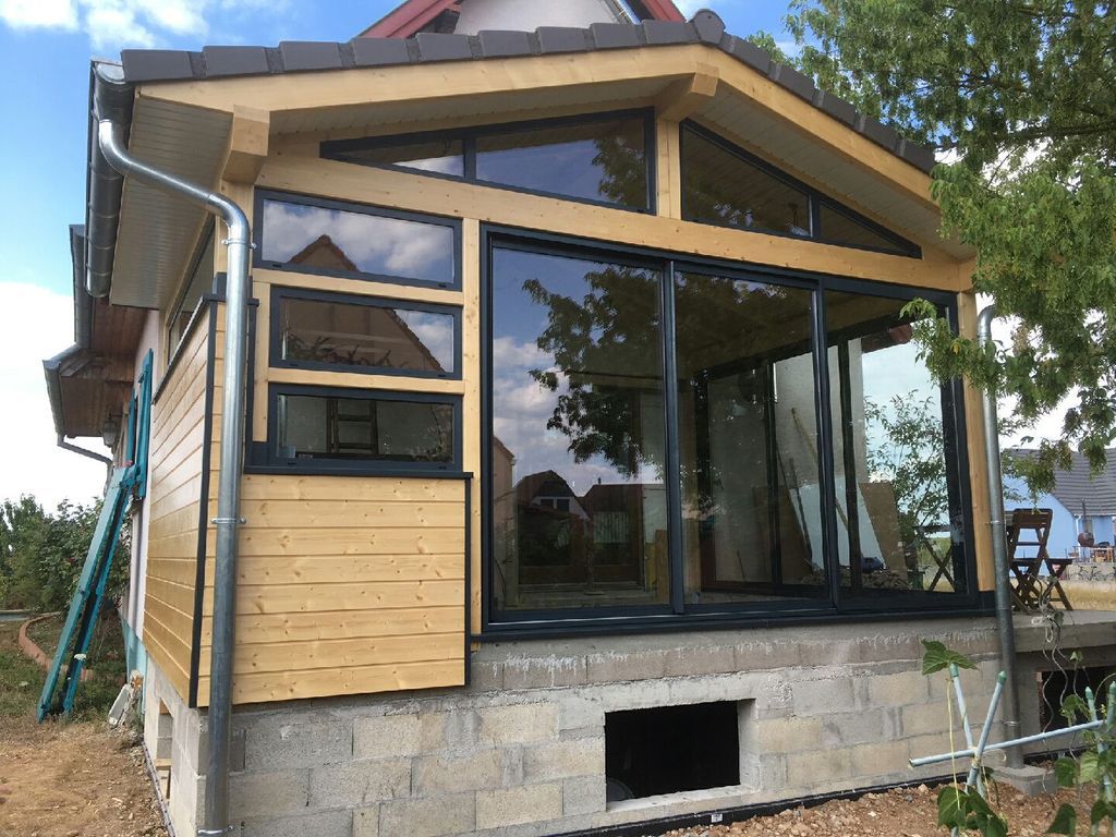 Extérieur de maison partiellement fini avec de grandes fenêtres, un bardage en bois et des fondations en pierre en construction