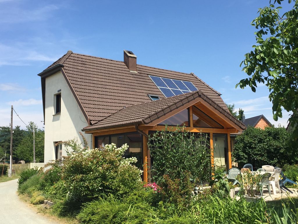 Maison avec panneaux solaires et porche en bois dans un jardin ensoleillé