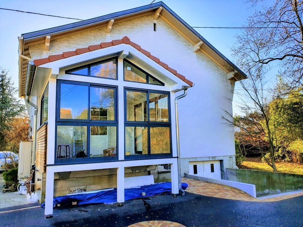 Maison blanche moderne avec une grande véranda vitrée et des finitions bleues dans un jardin ensoleillé