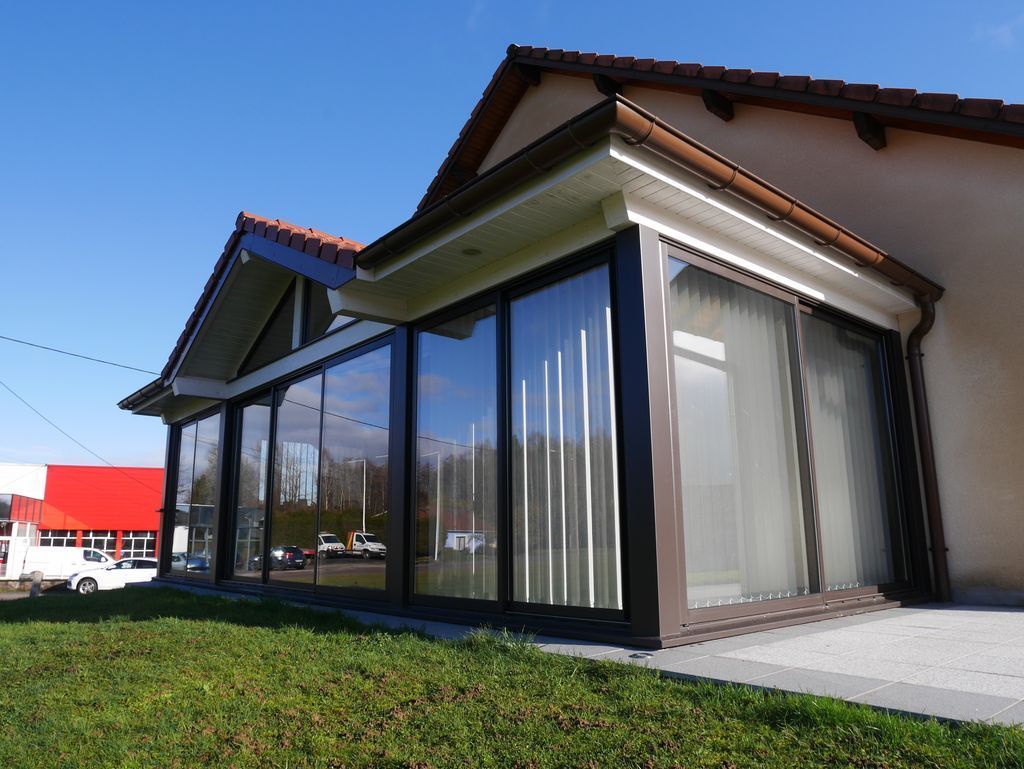 Maison moderne avec de grandes baies vitrées, un toit marron et une pelouse verte par une journée ensoleillée