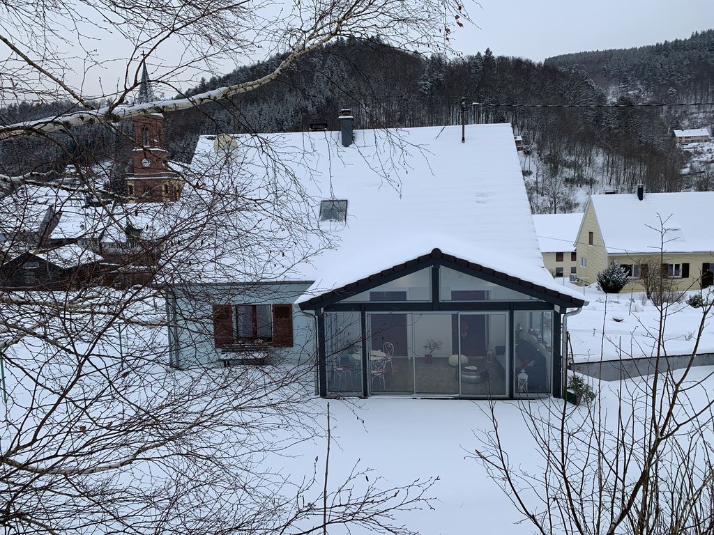 Maison enneigée avec une véranda vitrée dans un paysage rural hivernal