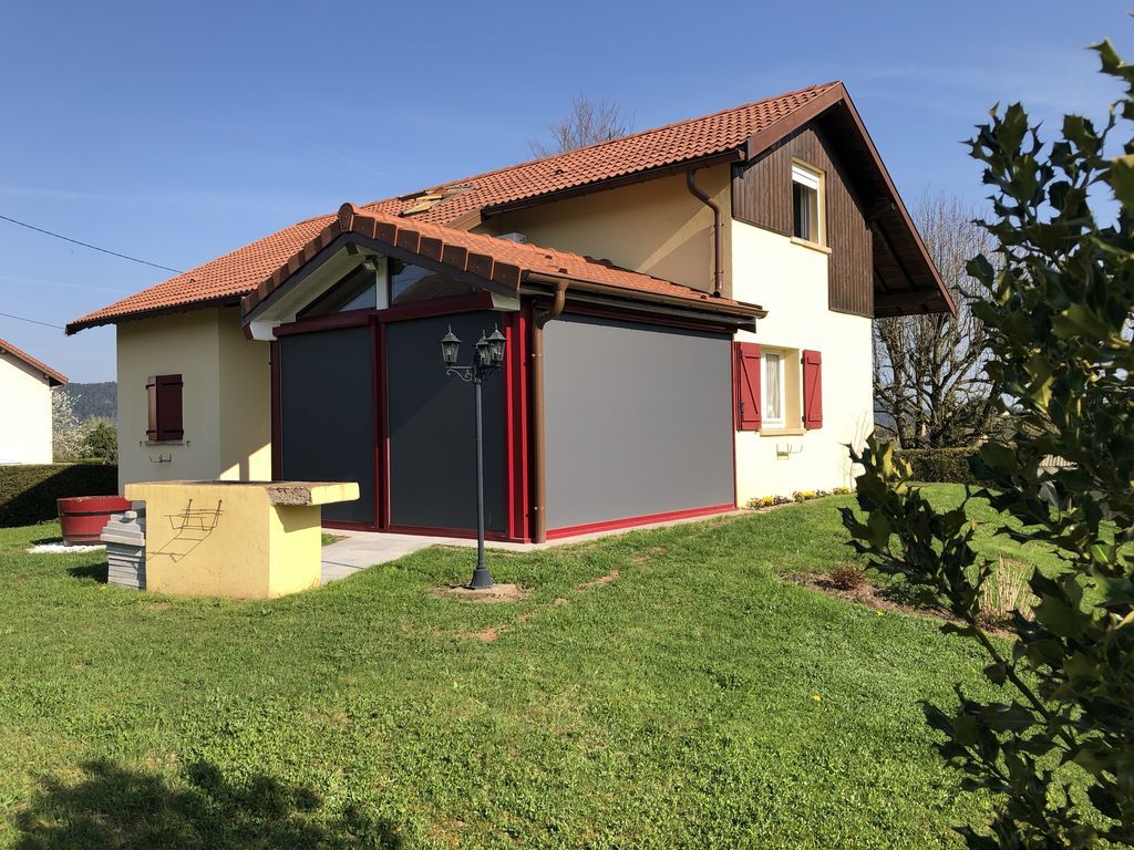 Petite maison crème et rouge avec un toit de tuiles et une cour gazonnée sous un ciel bleu clair