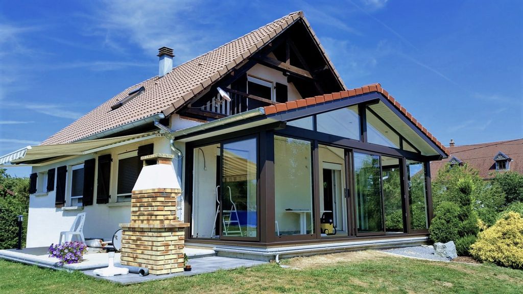 Maison moderne avec un toit de tuiles pentu et une véranda vitrée dans un jardin ensoleillé