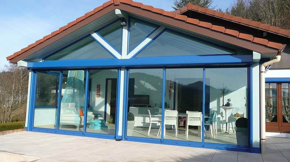 Façade en verre bleu d'une maison moderne avec de grandes fenêtres et un toit en tuiles rouges